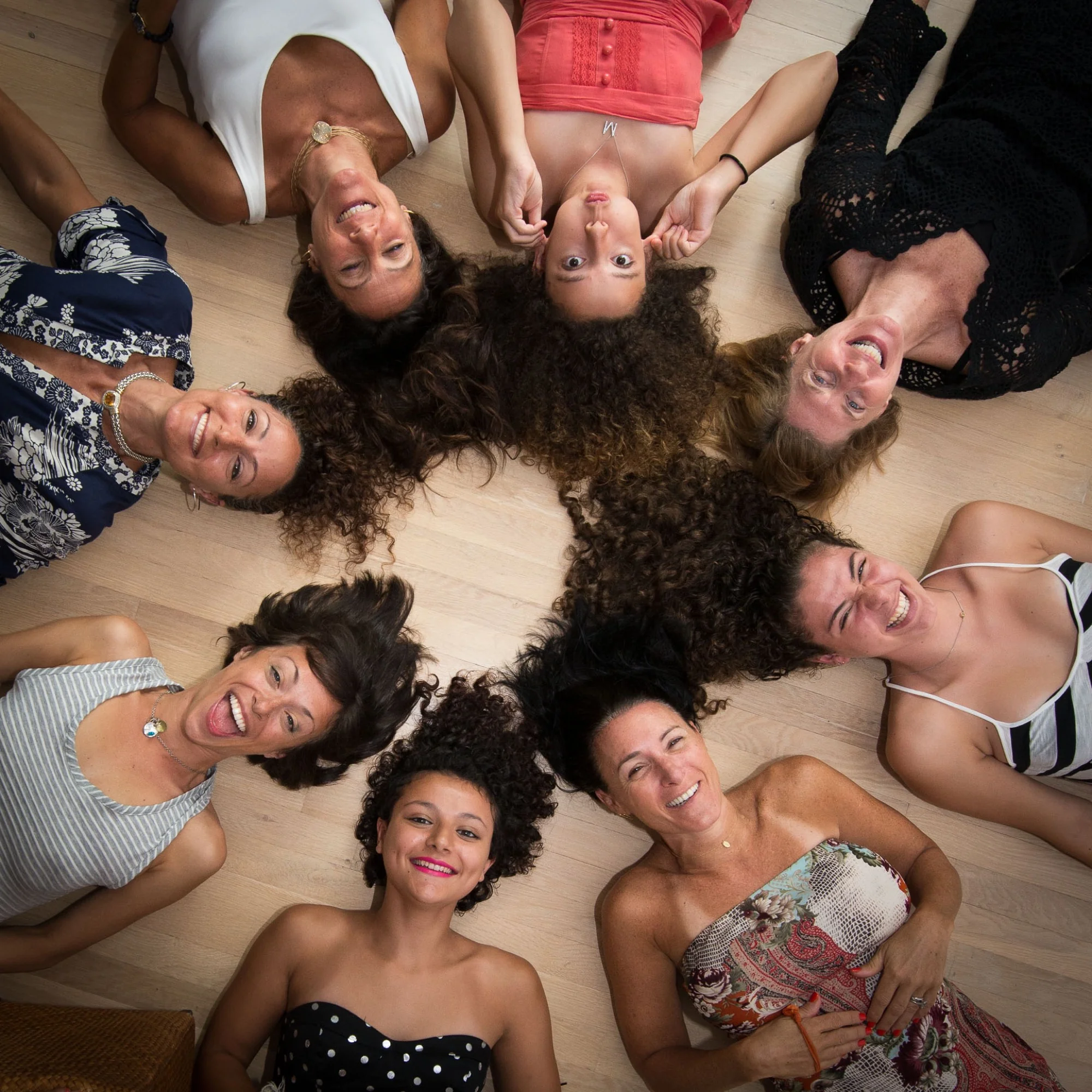 A group of women lying in a circle, laughing together, photographed from above at a retreat gathering